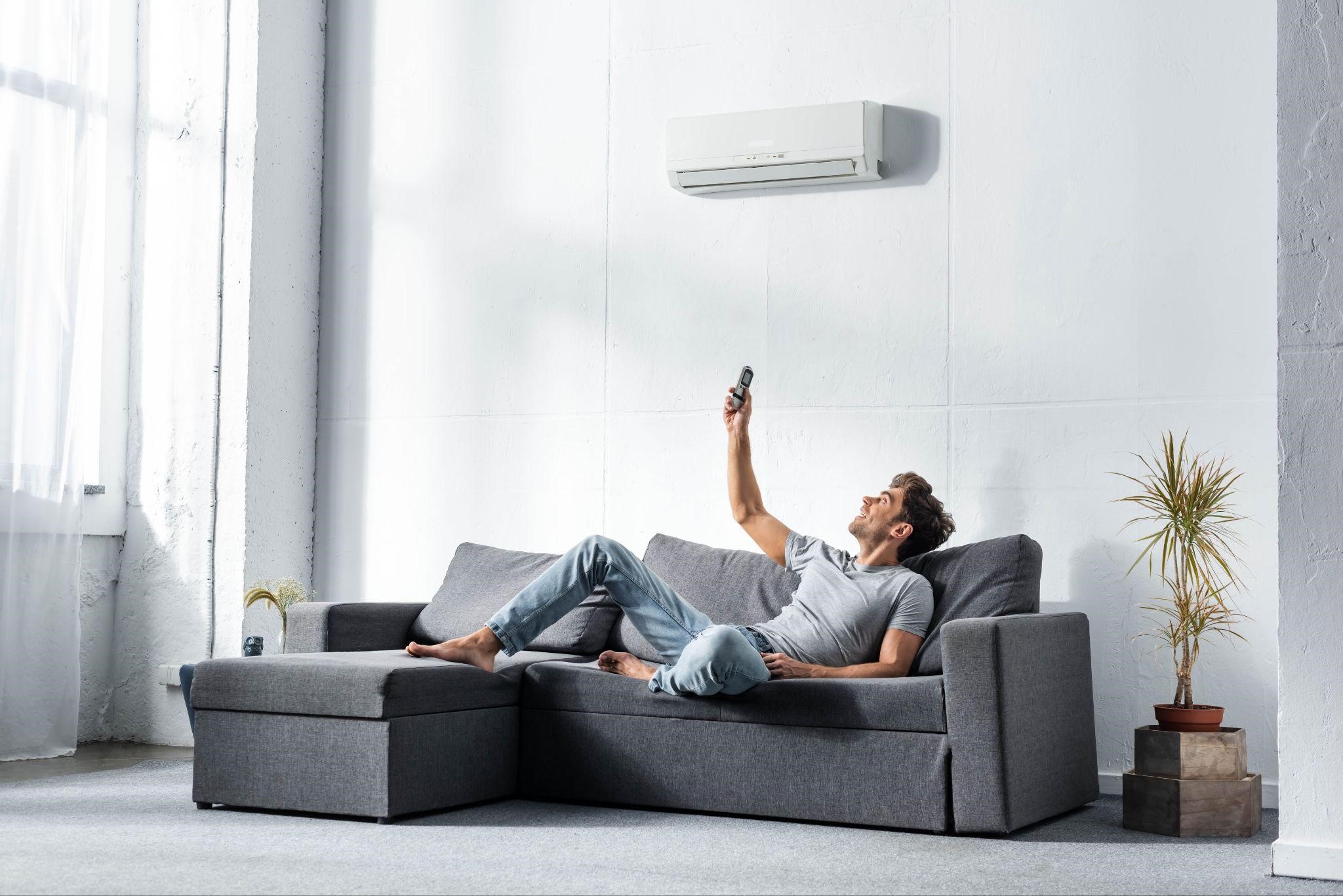 a man lying on sofa and switching on air conditioner